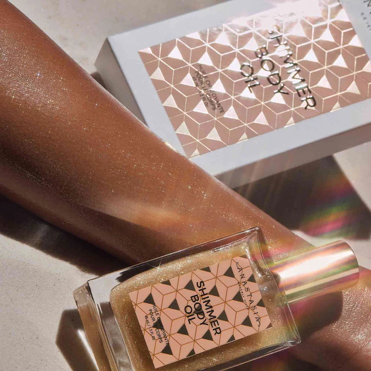 Shimmer body oil bottle on glowing skin with gold sparkles and matching geometric box