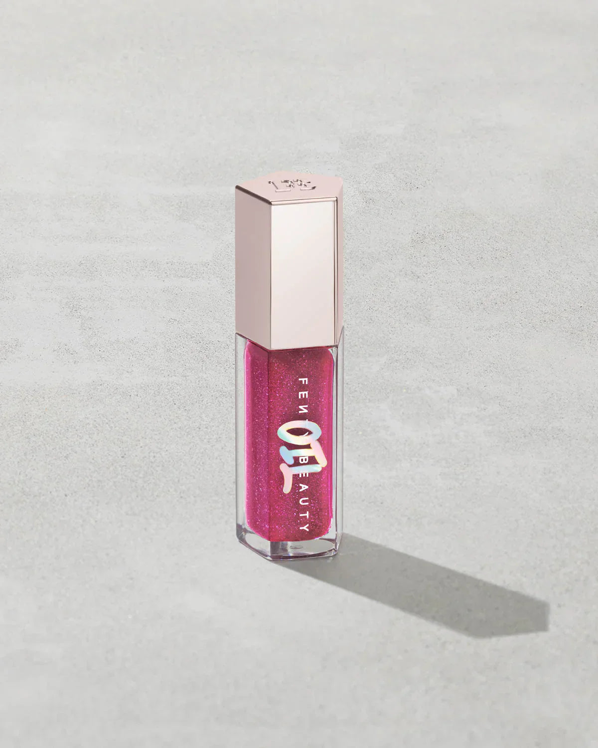 Fenty Beauty pink glitter liquid lip gloss with metallic cap on light textured surface