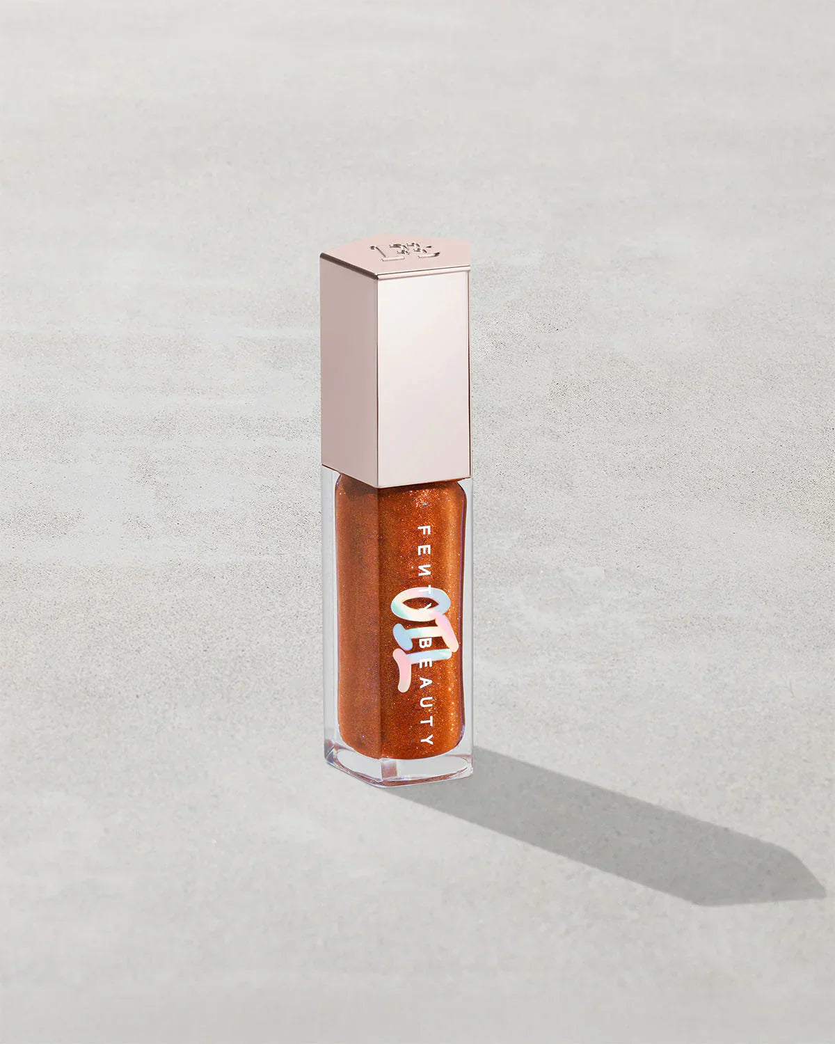Shimmery copper lip gloss in clear tube with metallic cap, Fenty Beauty label visible.