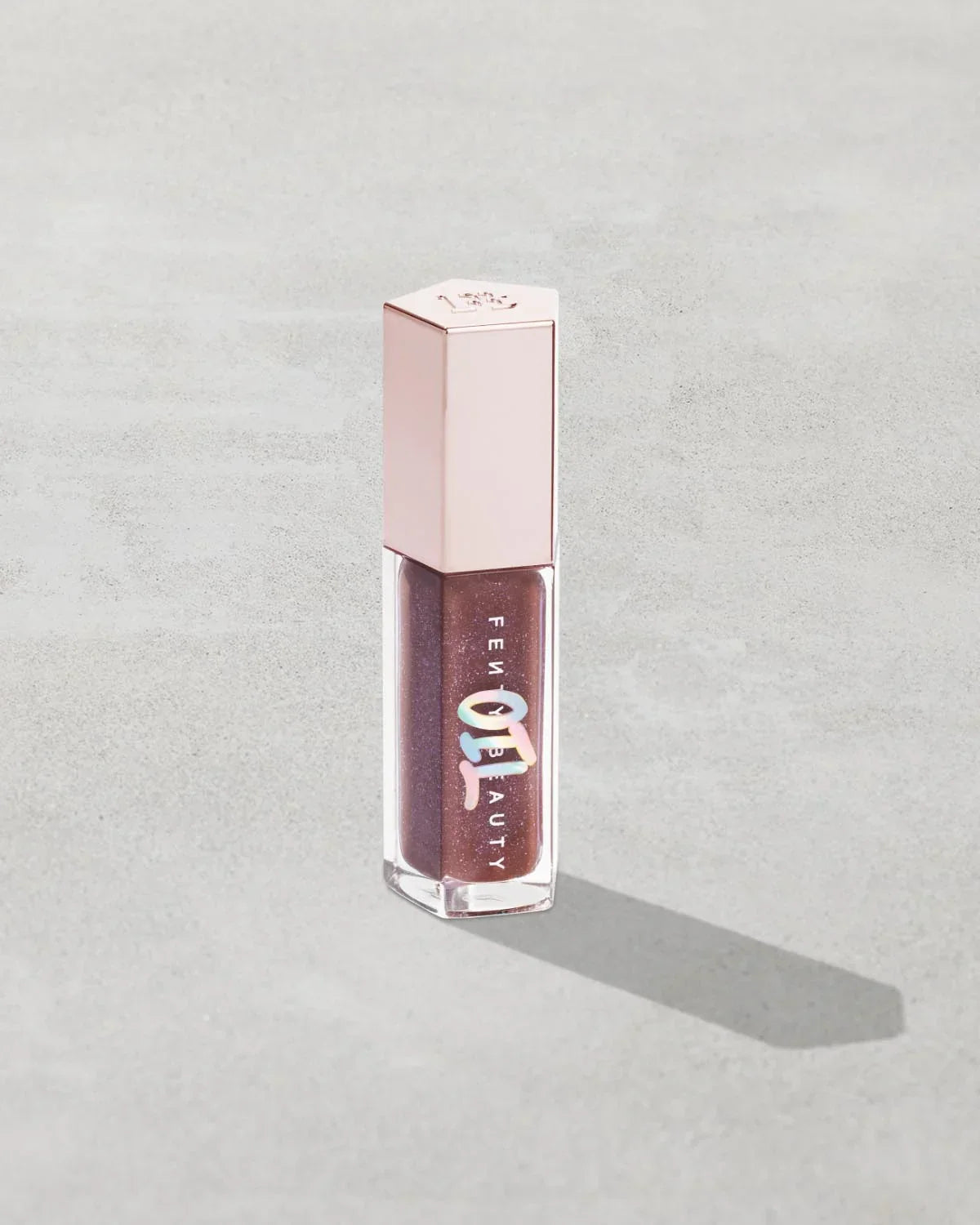 Rose amber liquid lip gloss in rose gold tube on a light grey background