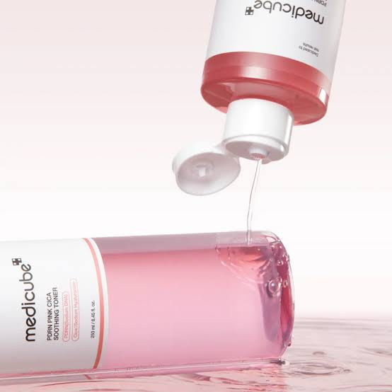 Pink soothing toner being poured from an open bottle, skincare product on white background
