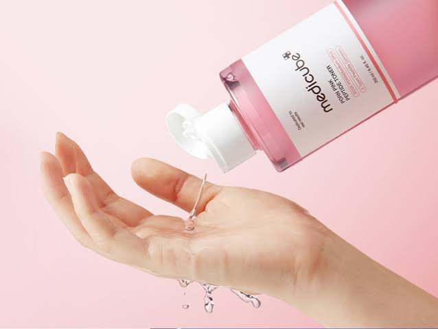 Hand applying Medlcube pink skincare toner liquid on palm, light pink background